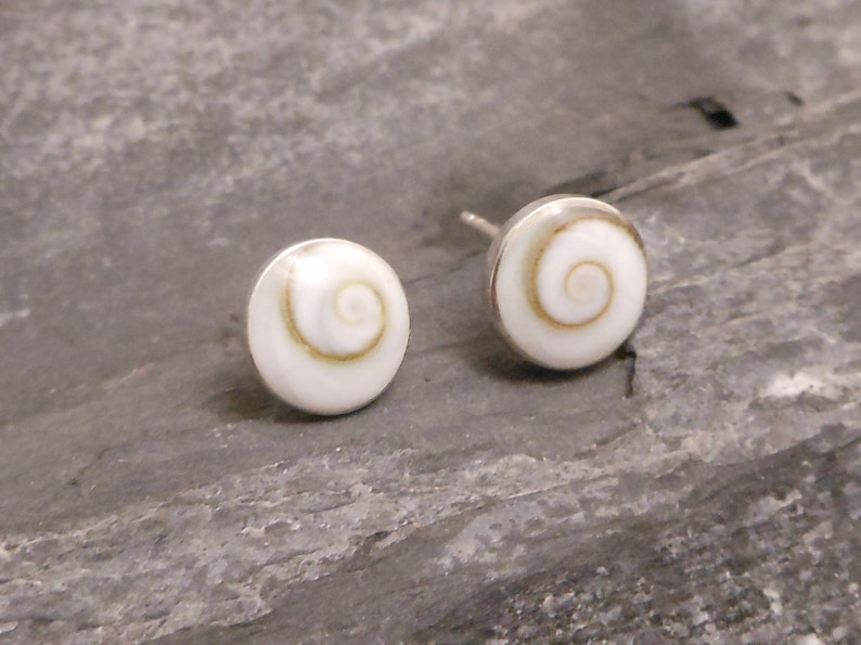 May include: A pair of silver stud earrings with white shell inlays featuring a spiral pattern.