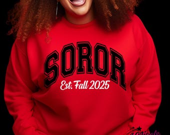 Puede incluir: Una sudadera roja con la palabra "SOROR" en letras negras con contorno blanco. Debajo está el texto "Est. Fall 2025" en blanco. La sudadera también tiene el texto "DESIGN #1" en un rectángulo rosa.