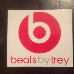 May include: A square white sticker featuring the Beats logo, a red circle with a white lowercase "b" inside. Below the logo, the text "beats by trey" is printed in red and gray.