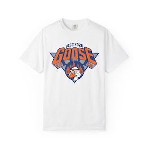 May include: A white short-sleeve t-shirt featuring a graphic print with the text MSG 2026, GOOSE, 6.19, and 6.20. The design includes a blue triangle, a circular city skyline silhouette, and a cartoon goose wearing an orange and blue headband.