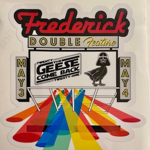 May include: A vintage movie theater marquee with the text "Frederick Double Feature" and the films "Twenty-One The Geese Come Back" and "Star Wars" playing on May 3rd and 4th. The marquee is surrounded by colorful spotlights.
