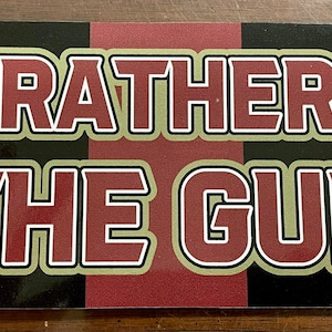 May include: A red and black striped sticker with the text "I'd rather be in the Gulch" in gold letters with a white outline.