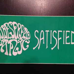 May include: A green sticker with white text that reads "Widespread Panic Satisfied..." The text is in a stylized font.