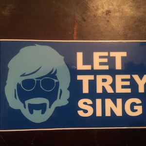 May include: Blue and white sticker with a silhouette of a person with a beard and sunglasses. The text "LET TREY SING" is printed in white on the sticker.