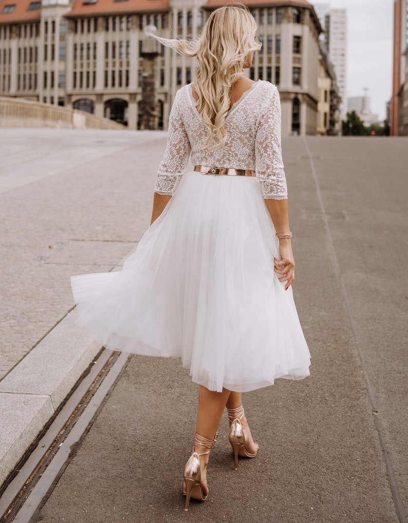 May include: A white tulle skirt with a lace top and a gold belt. The skirt is flowing and the woman is walking on a paved street.