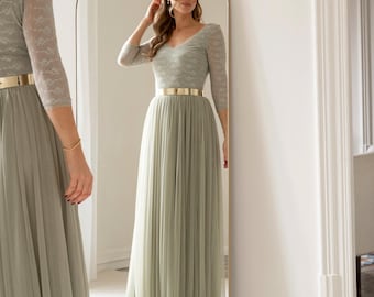 May include: A floor-length sage green dress featuring a V-neckline, three-quarter length lace sleeves, and a pleated tulle skirt. The dress is accented with a smooth, metallic gold belt at the waist, creating a distinct contrast between the bodice and skirt.