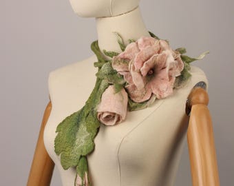May include: A handcrafted felt floral accessory featuring a large pink flower, a rose bud, and green leaves. The floral arrangement is displayed on a mannequin, showcasing the intricate details and textures of the felted design.