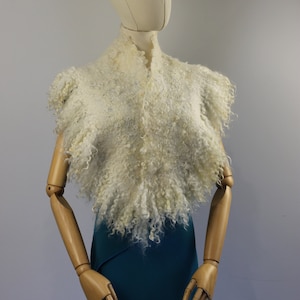 Peut inclure: Un châle blanc et moelleux avec un design texturé et bouclé. Le châle est drapé sur un mannequin portant une jupe turquoise.