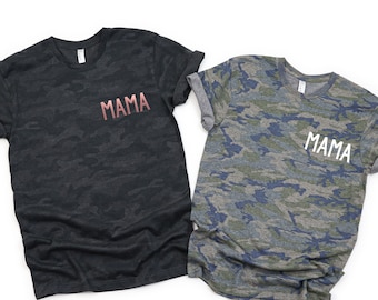May include: Two camouflage t-shirts with the word "MAMA" printed on the front. One shirt is black and the other is blue and green.