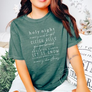 May include: A green t-shirt with white text that reads "holy night merry and bright sleigh bells gingerbread peace on earth let it snow cookies.presents.tree. merry christmas".