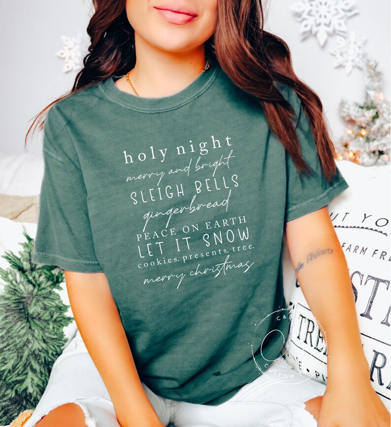 May include: A green t-shirt with white text that reads "holy night merry and bright sleigh bells gingerbread peace on earth let it snow cookies.presents.tree. merry christmas".