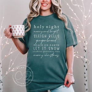 May include: Teal blue t-shirt with white text that reads "holy night merry and bright sleigh bells gingerbread peace on earth let it snow cookies, presents, tree. merry christmas"