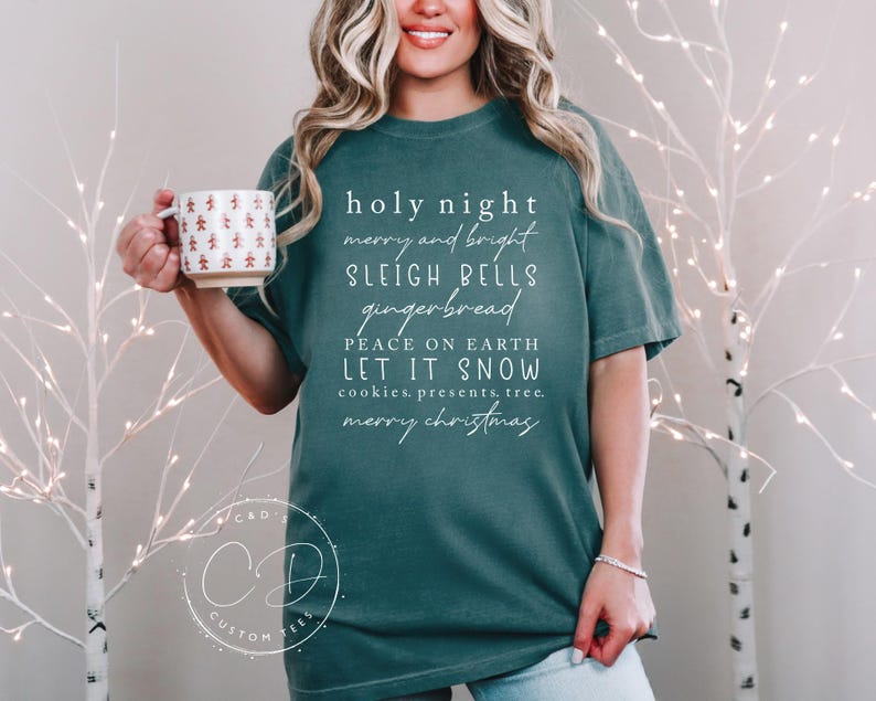 May include: Teal blue t-shirt with white text that reads "holy night merry and bright sleigh bells gingerbread peace on earth let it snow cookies, presents, tree. merry christmas"