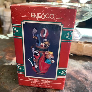 May include: A red and white golf bag ornament with a mouse wearing a blue shirt and a yellow hat. The ornament is part of the "Sports Star" series and is labeled "Tee-riffic Holidays".
