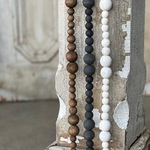 May include: Three strands of wooden bead garland in brown, black, and white. The garlands are hanging on a wooden post.