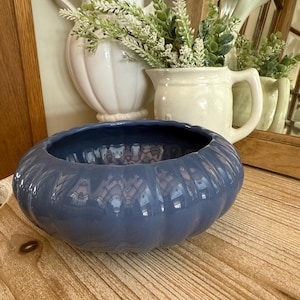 May include: A blue ceramic bowl with a rounded, slightly rippled design. The bowl is sitting on a wooden surface.