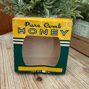 May include: A vintage yellow and green box for Pure Comb Honey. The box has a honeycomb pattern and the words "Pure Comb Honey" printed on the front. The box has a rectangular opening.