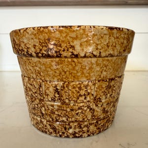 May include: A large, speckled brown and tan ceramic planter. The planter has a wide rim and a textured, basket-weave design around the body. The speckled pattern gives it a rustic, vintage appearance. Ideal for indoor or outdoor use.