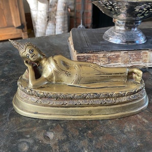 May include: A gold-colored reclining Buddha statue with a detailed face and intricate design on the base.
