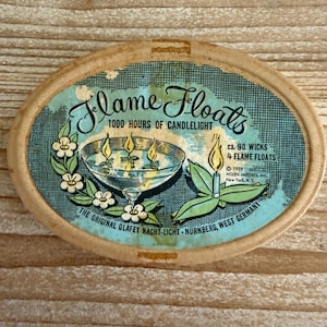 May include: An oval-shaped vintage box for "Flame Floats" with text and illustrations. The box features a teal background with a drawing of a glass bowl with floating candles. Text includes "1000 hours of candlelight" and "ca. 90 wicks - 4 flame floats."