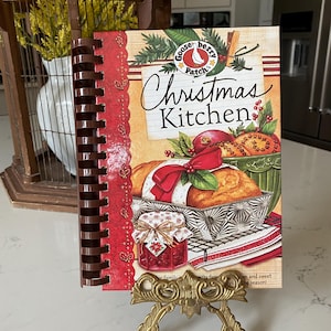 May include: A red and green cookbook with a festive Christmas theme. The cover features a goose illustration and the title "Gooseberry Patch's Christmas Kitchen".