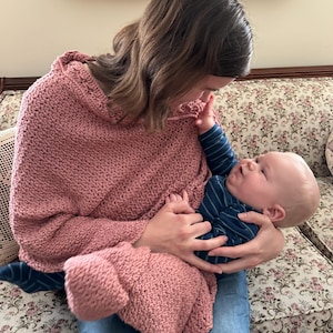 May include: A dusty rose crocheted nursing cover and matching blanket. The cover is draped over the shoulders, and the blanket is wrapped around a baby. The baby wears a blue and navy striped top.