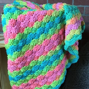 May include: A colorful crocheted baby blanket with a textured, wave-like pattern in shades of pink, green, and blue.