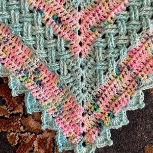 May include: A crocheted baby blanket with a light blue and pink color scheme. The blanket has a scalloped edge and a woven pattern.