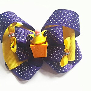 May include: A purple and yellow polka dot hair bow with a small yellow frog toy in the center.