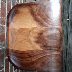 May include: A large, wooden serving tray with a natural wood finish. The tray has a rounded, organic shape and is made from a single piece of wood.