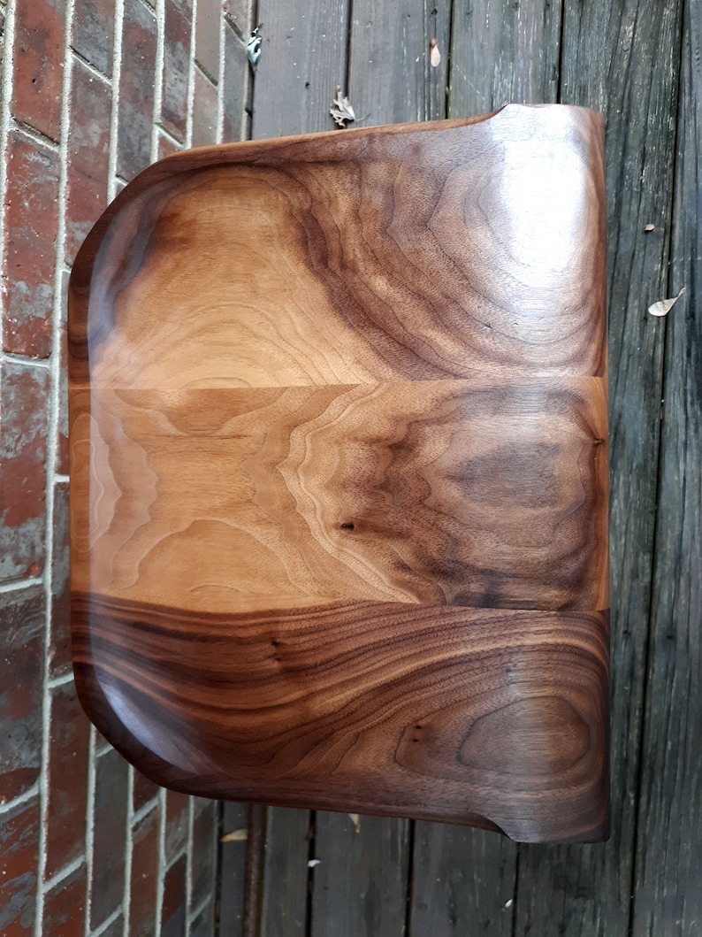 May include: A large, wooden serving tray with a natural wood finish. The tray has a rounded, organic shape and is made from a single piece of wood.