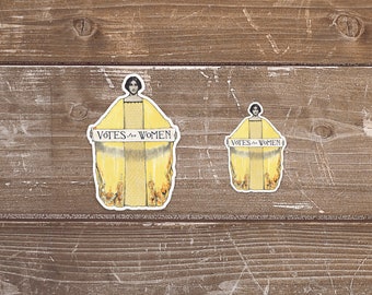 May include: Two vintage-style stickers featuring a woman in a yellow robe holding a banner that reads "Votes for Women".