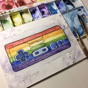 May include: Watercolor painting of a rainbow-colored video game controller with a black outline. The controller has a rainbow design with the colors red, orange, yellow, green, blue, indigo, and violet. The painting is signed "Liv 4/10/2019".