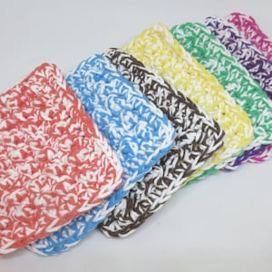 May include: A set of seven crocheted dishcloths in various colors, including coral, blue, brown, yellow, green, purple, and pink. Each dishcloth is made with a white and colored yarn, creating a textured pattern.