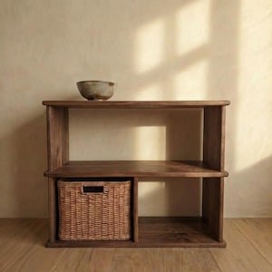 May include: A dark brown wooden bookshelf with two shelves and a woven basket. A small, round, speckled bowl sits on the top shelf. The basket is rectangular with a handle cutout. The bookshelf is made of solid wood.