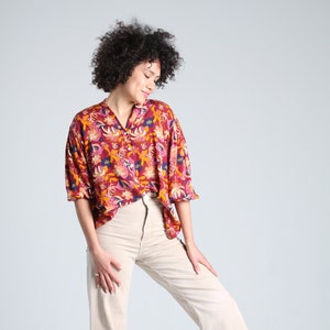May include: A woman wearing a red and yellow floral print button-up shirt with a white pair of wide-leg pants.