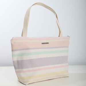 May include: A striped canvas tote bag with a zipper closure and two handles. The bag is in shades of pink, yellow, green, and purple.