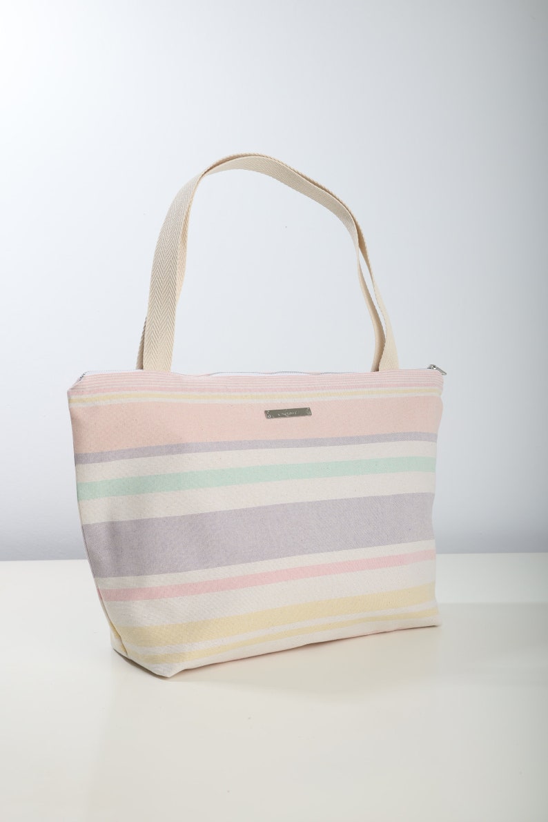 May include: A striped canvas tote bag with a zipper closure and two handles. The bag is in shades of pink, yellow, green, and purple.