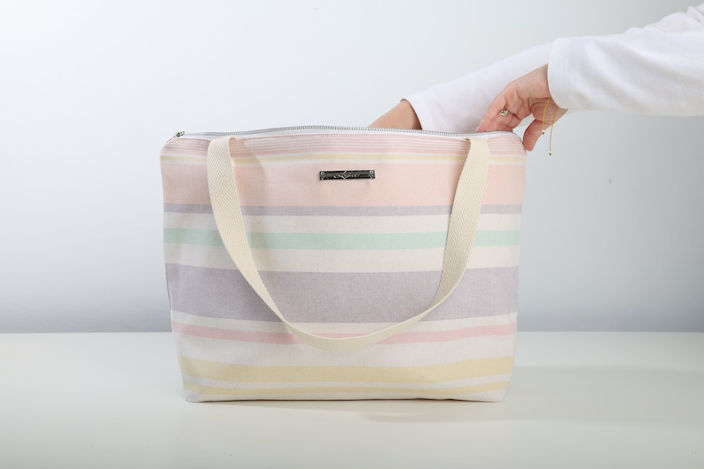 May include: A striped tote bag with a zipper closure and two canvas straps. The bag is made of a soft, light-colored fabric with pastel stripes in pink, yellow, green, and gray.