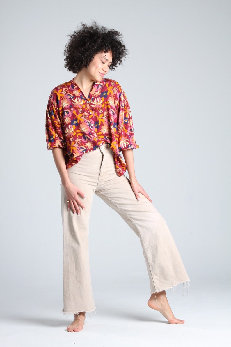 May include: A woman wearing a red and yellow floral print button-up shirt with a white pair of wide-leg pants.