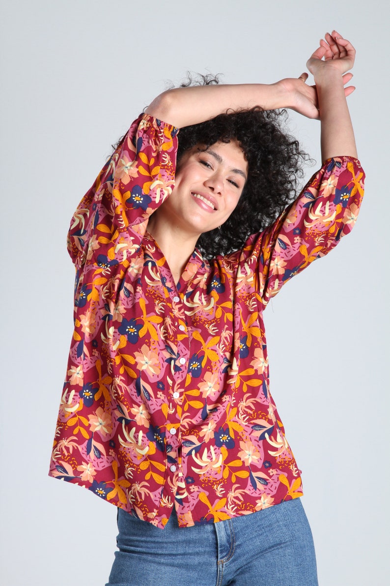 May include: A red, pink, yellow, and blue floral print button-up shirt with long sleeves. The shirt has a relaxed fit and a slightly cropped length.