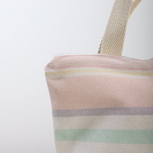 May include: A striped tote bag with a pink, white, and green color scheme. The bag has a zipper closure and a canvas strap.