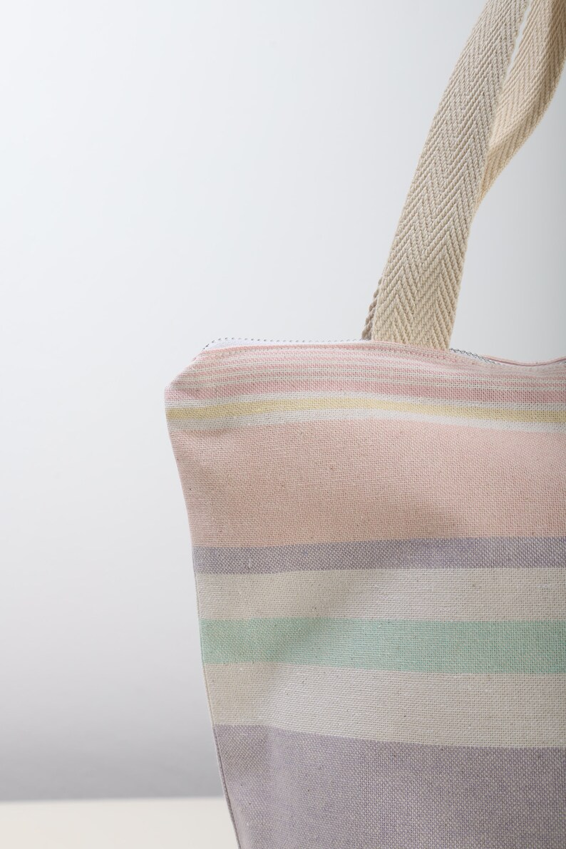 May include: A striped tote bag with a pink, white, and green color scheme. The bag has a zipper closure and a canvas strap.