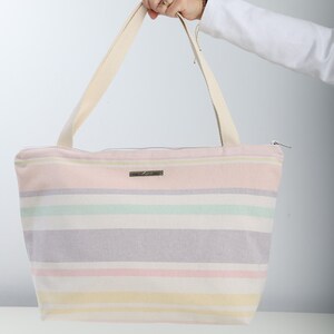 May include: A striped canvas tote bag with a zipper closure and two long handles. The bag is pink, yellow, green, and purple.