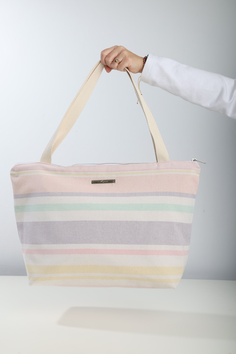 May include: A striped canvas tote bag with a zipper closure and two long handles. The bag is pink, yellow, green, and purple.