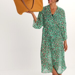 May include: A woman wearing a green and brown leopard print robe holds a mustard yellow tote bag with brown leather handles.