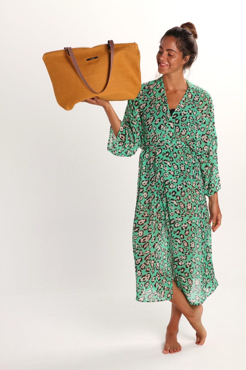 May include: A woman wearing a green and brown leopard print robe holds a mustard yellow tote bag with brown leather handles.