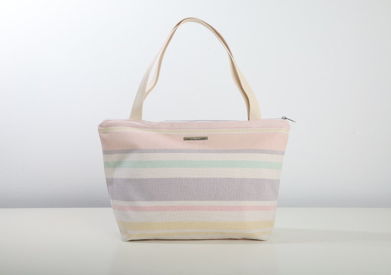 May include: A striped tote bag with a zipper closure. The bag is made of canvas and has a light pink, yellow, green, and purple striped pattern.