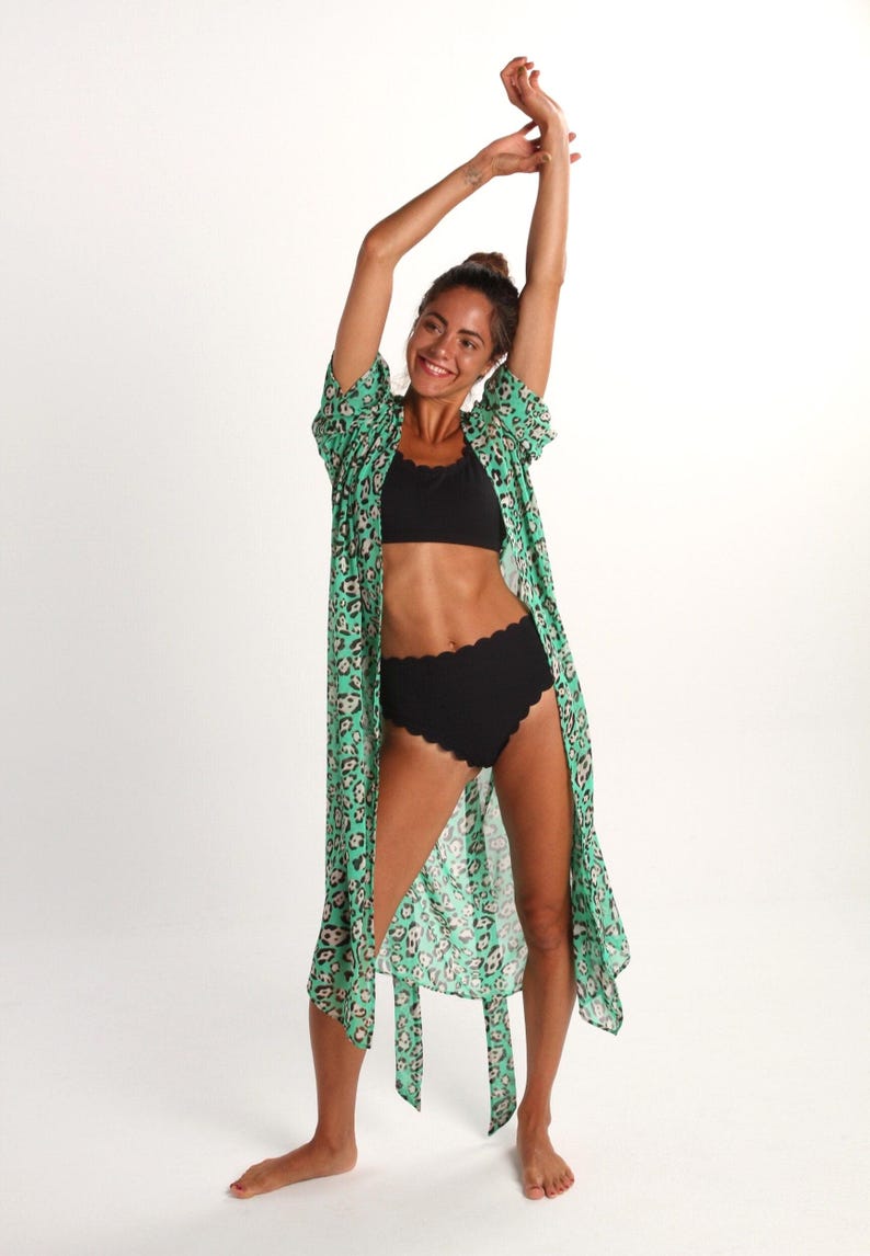 May include: A woman wearing a green and brown leopard print kimono with a black bikini top and high-waisted black bikini bottoms.