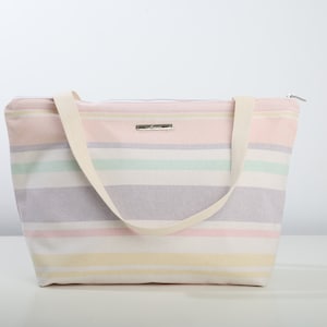 May include: A striped tote bag with a zipper closure and two fabric handles. The bag is made of a light-colored canvas with stripes of pink, yellow, green, and purple.